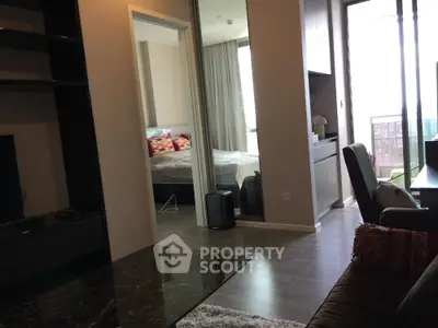 Modern apartment interior with open living room and bedroom view, featuring sleek furniture and natural light.