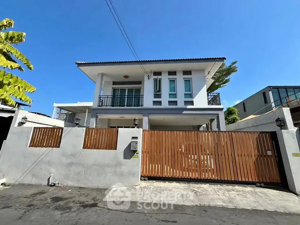 Modern two-story house with gated entrance and balcony in a sunny neighborhood.