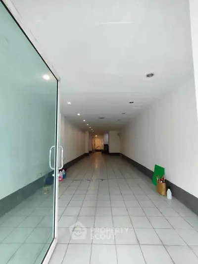 Spacious empty commercial space with tiled flooring and glass entrance, ideal for retail or office use.