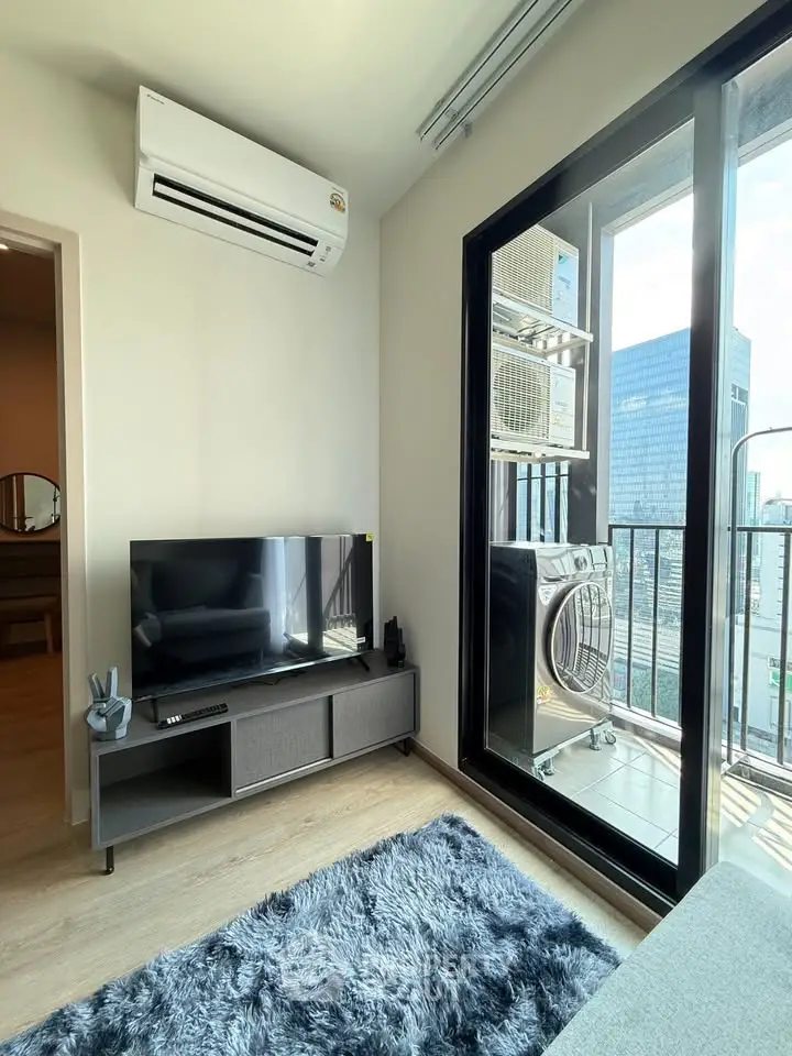 Modern living room with balcony view and washing machine, featuring sleek TV setup and air conditioning.
