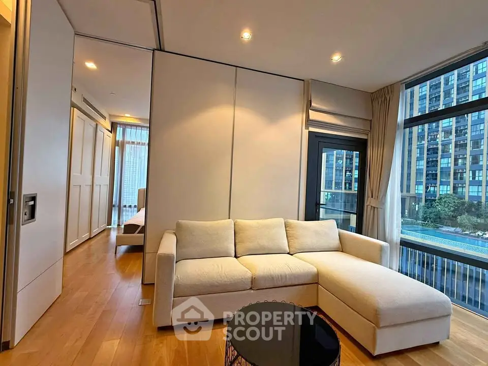 Modern living room with large windows and city view, featuring a cozy beige sofa and wooden flooring.
