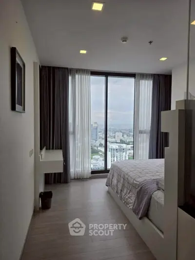 Modern bedroom with large window offering stunning city view in high-rise apartment.