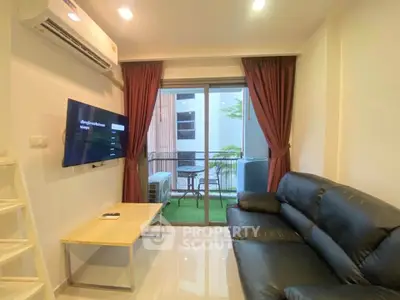 Modern living room with balcony view, featuring sleek black leather sofa and wall-mounted TV.