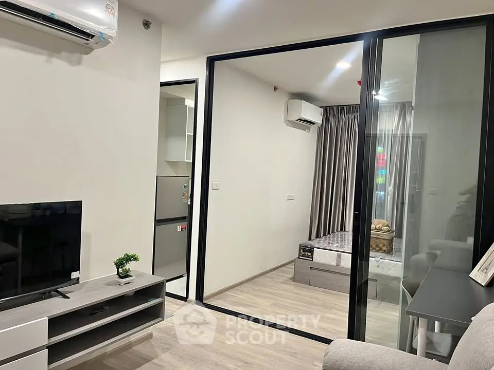 Modern apartment with open layout, featuring a cozy living area and bedroom separated by glass doors.