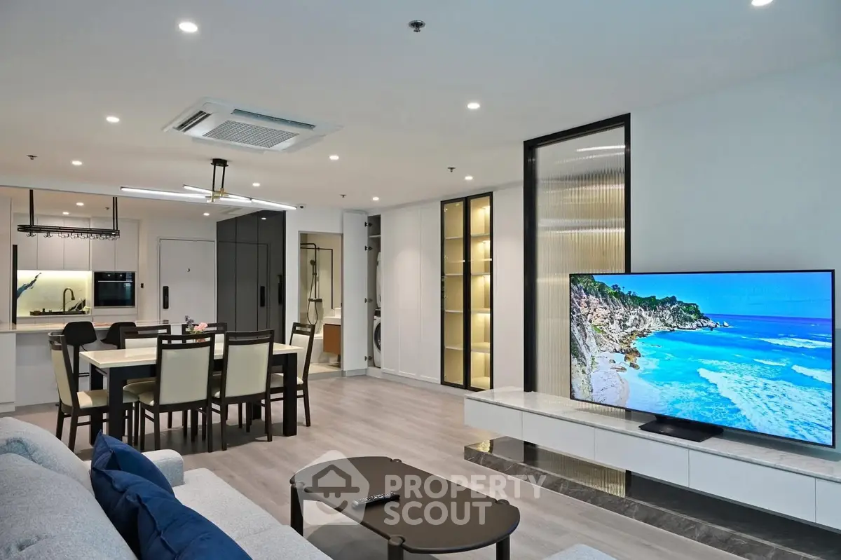 Spacious modern living room with open kitchen and large TV, perfect for entertaining.