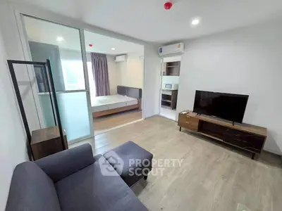 Modern living room with sleek furniture and open view into bedroom, featuring contemporary design and ample natural light.