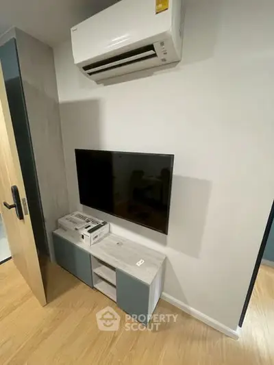Modern living room with wall-mounted TV and air conditioning unit, featuring sleek storage cabinet.