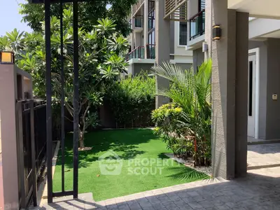 Charming garden entrance with lush greenery and modern building facade, perfect for serene living.