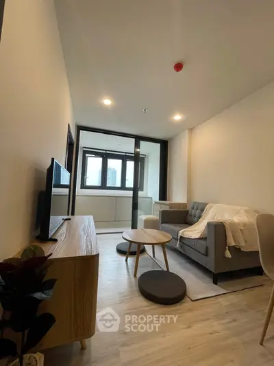 Modern living room with cozy sofa and TV, featuring sleek wooden furniture and large windows.