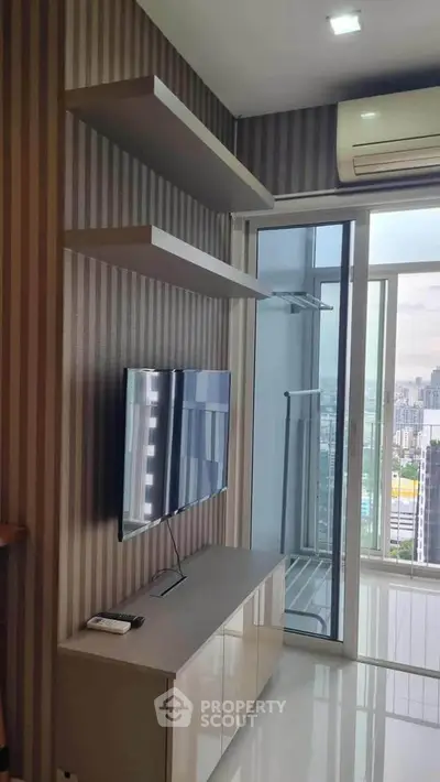 Modern living room with sleek TV setup and city view balcony in high-rise apartment.