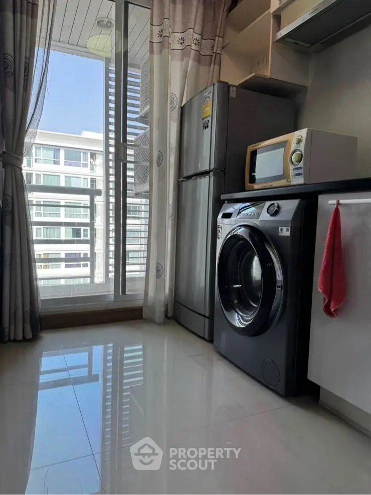 Modern kitchen with washing machine, fridge, and microwave in a high-rise apartment.