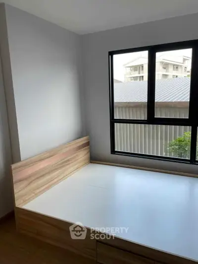 Cozy bedroom with modern wooden bed frame and large window offering natural light and urban view.