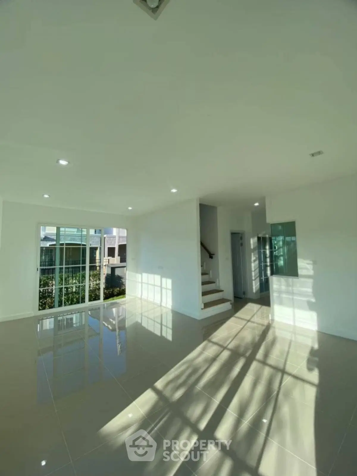 Spacious sunlit living room with glossy tiled floors and modern staircase.