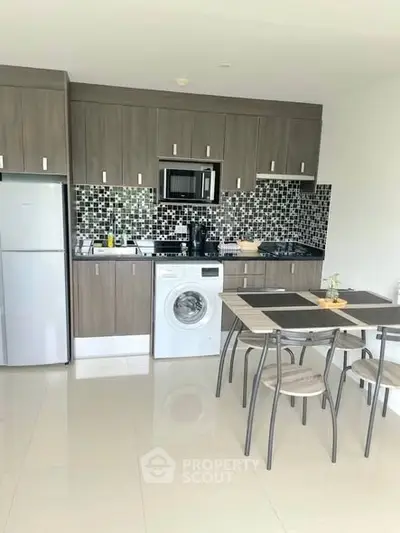 Modern kitchen with sleek cabinetry, washing machine, and dining area in open layout.