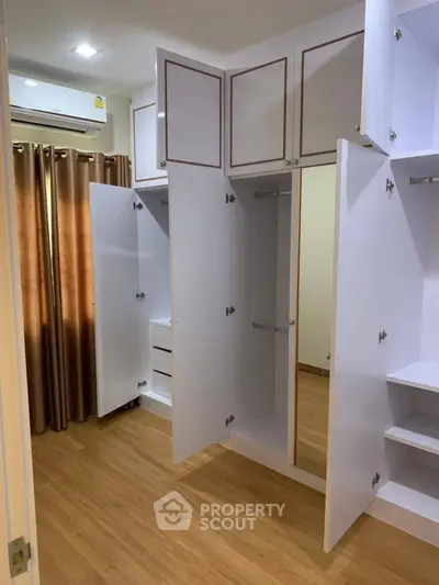 Spacious bedroom with open white wardrobes and wooden flooring