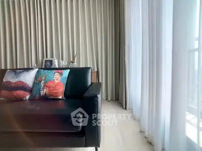 Stylish living room with modern black sofa and artistic decor, featuring floor-to-ceiling curtains and bright natural light.