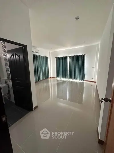Spacious empty room with glossy tiled floors and large windows, ideal for customization.