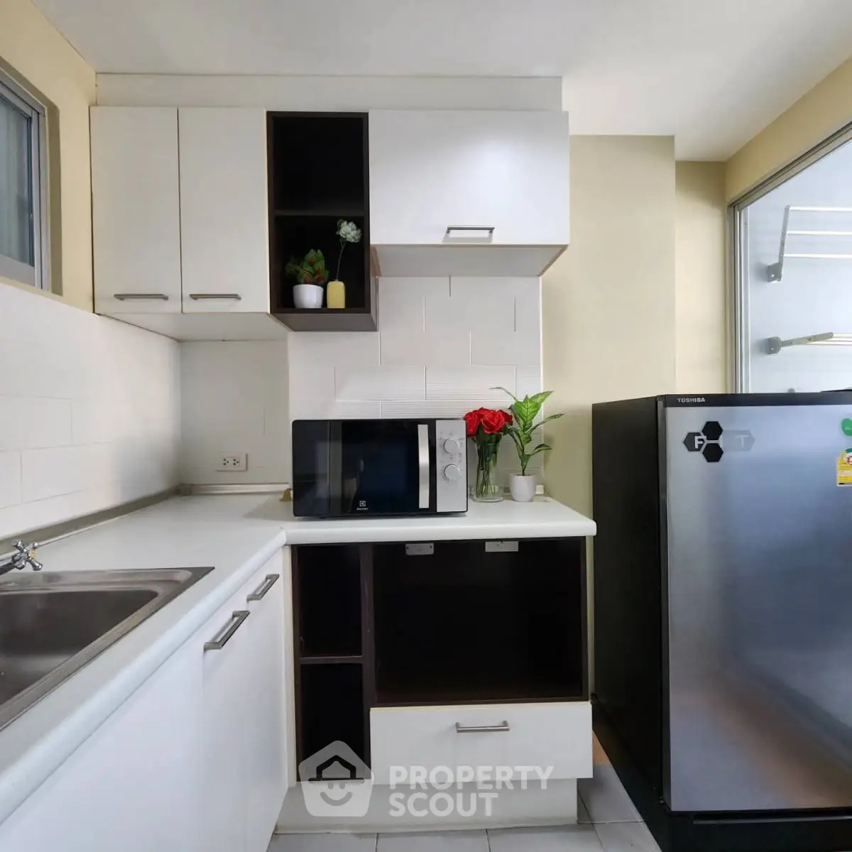 Modern kitchen with sleek white cabinets, stainless steel fridge, and microwave, perfect for urban living.