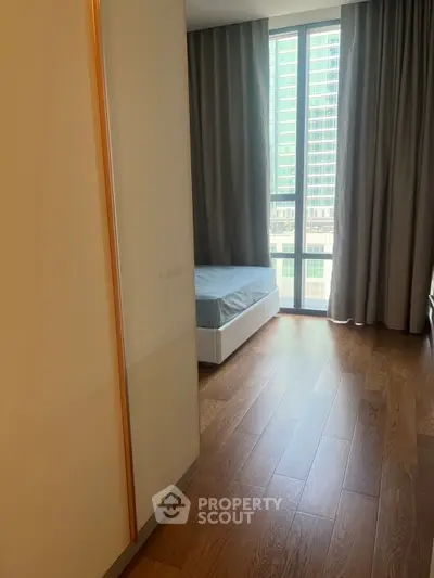 Modern bedroom with large window and wooden flooring in urban apartment