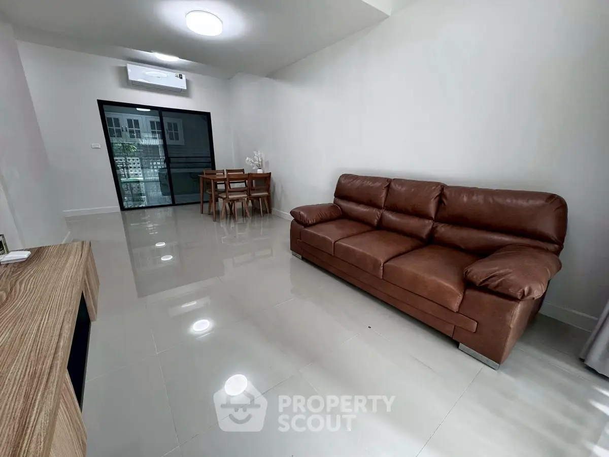 Spacious modern living room with leather sofa and dining area, featuring sleek tile flooring and large window.