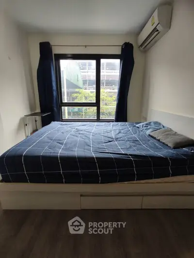 Cozy bedroom with large window and modern air conditioning unit, perfect for urban living.