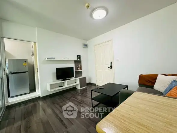 Modern living room with sleek flooring and cozy furnishings, adjacent to a compact kitchen area.
