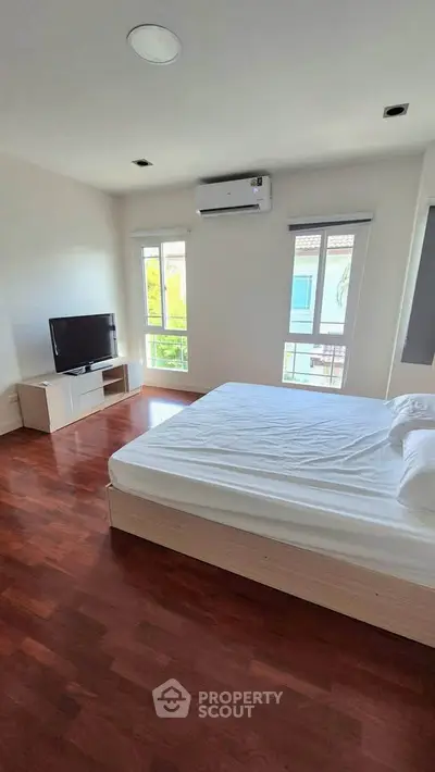 Spacious bedroom with hardwood floors, large windows, and modern furnishings.