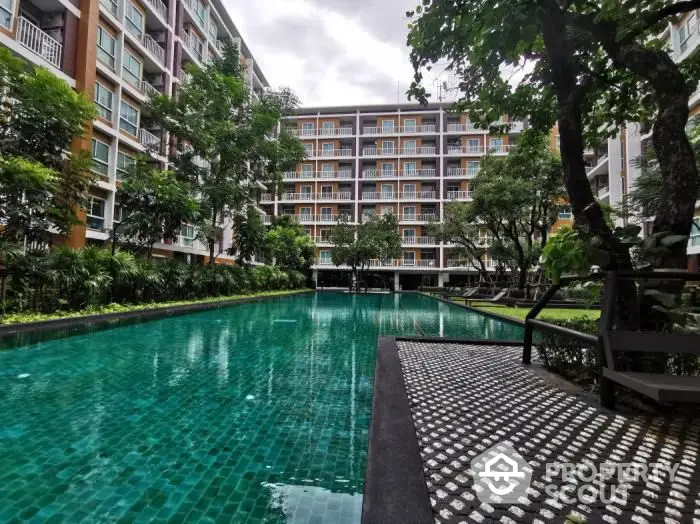 Lush greenery surrounds a tranquil pool area, offering a serene oasis amidst a modern residential complex with ample lounging spaces.