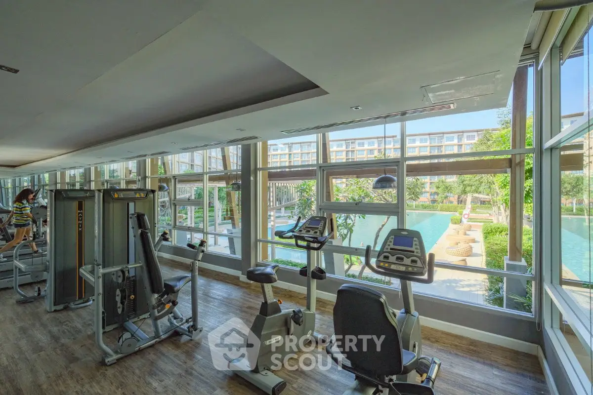 Spacious gym with modern equipment and pool view in luxury apartment complex.