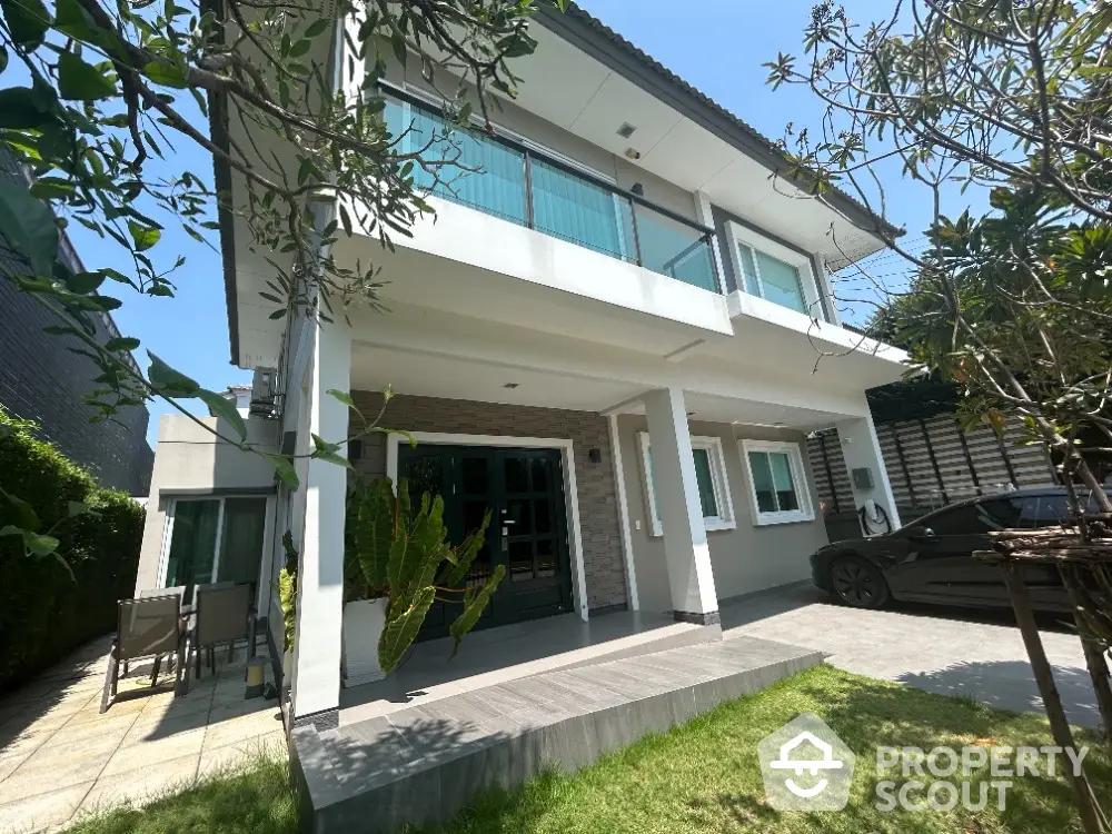 Spacious two-story home with large windows and a welcoming porch, nestled in a lush green garden, offering a serene suburban living experience.