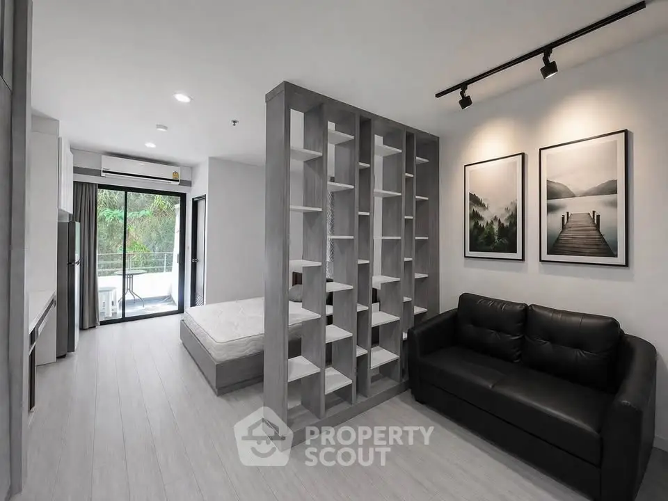 Modern studio apartment with stylish partition, cozy sofa, and scenic artwork, offering a serene living space.