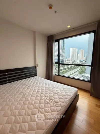 Spacious bedroom with large window offering stunning city view in modern apartment.