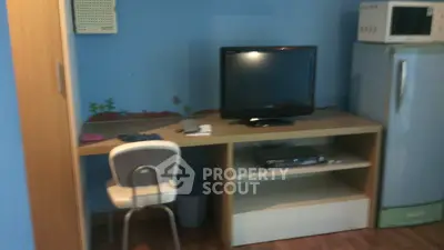Cozy study area with desk, chair, TV, and microwave in a compact space.