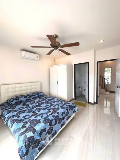 Spacious bedroom with modern decor and ensuite bathroom, featuring a ceiling fan and stylish bedding.
