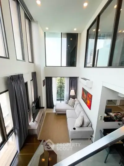 Spacious modern living room with high ceilings and large windows, featuring a cozy sectional sofa and stylish decor.