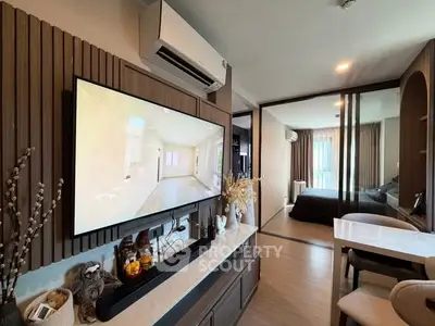 Modern living room with stylish decor and large TV, leading to a cozy bedroom through sliding glass doors.