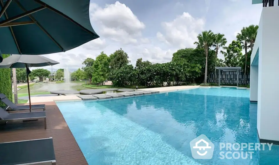 Luxurious outdoor pool with serene garden view and sun loungers, perfect for relaxation.