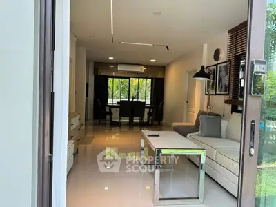 Modern living room with sleek furniture and dining area, featuring large windows and natural light.