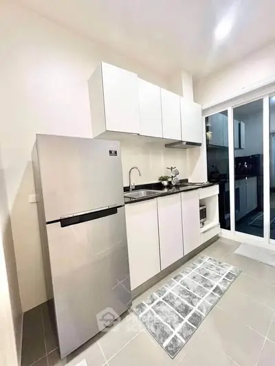 Modern kitchen with sleek white cabinets and stainless steel fridge in a bright, contemporary apartment.