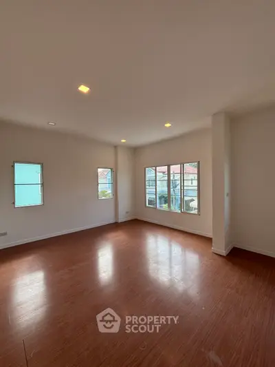 Spacious empty living room with large windows and wooden flooring, perfect for customization.