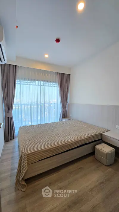Spacious bedroom with large window and modern decor in a high-rise apartment.