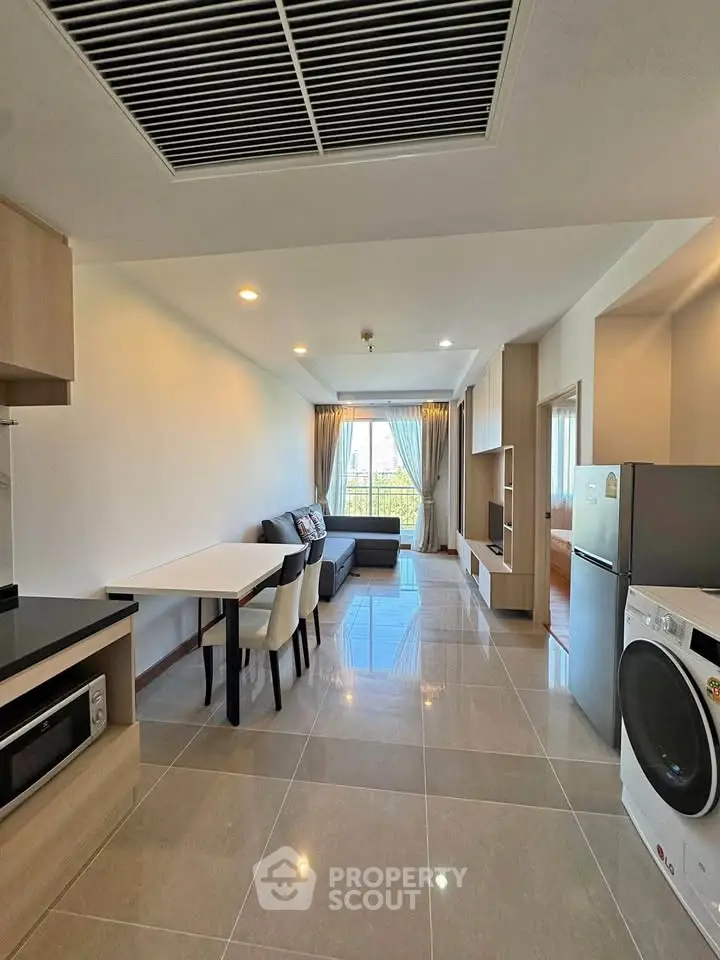 Modern open-plan living room with sleek kitchen and dining area, featuring large windows and stylish furnishings.