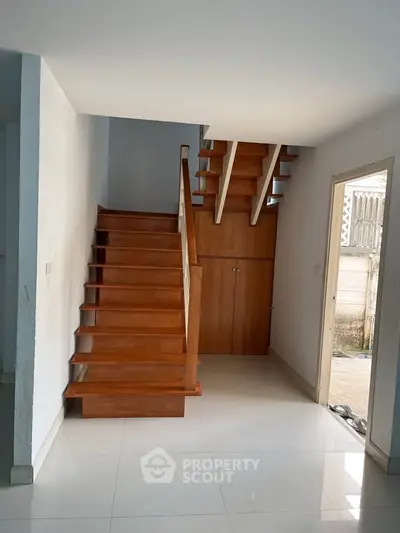 Modern wooden staircase in a bright, minimalist interior with white tiled flooring.
