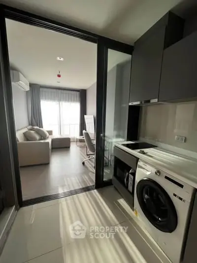 Modern apartment with sleek kitchen and cozy living room, featuring natural light and stylish furnishings.