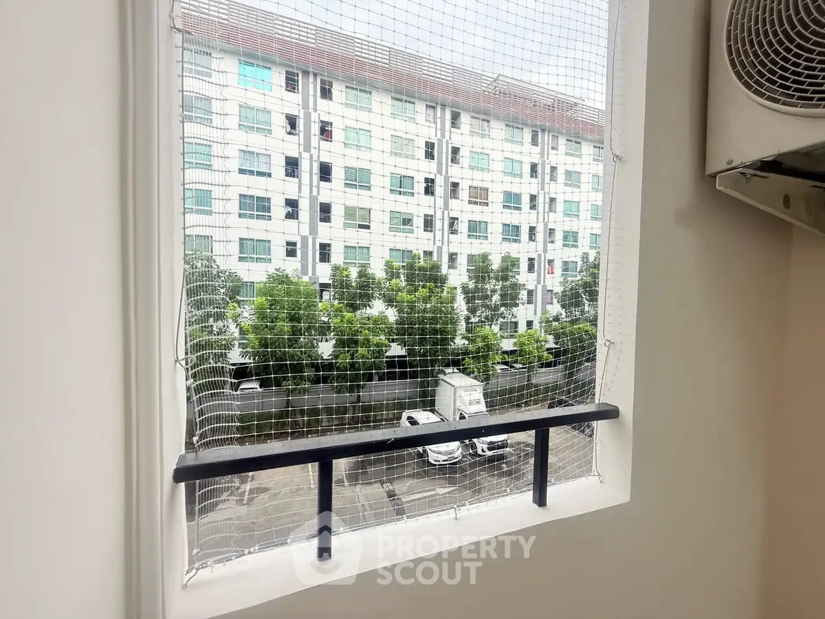 View from a window with safety netting overlooking a residential building and parking area.