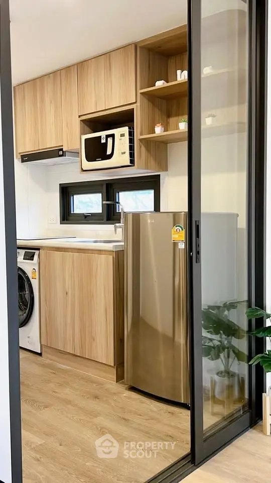 Modern kitchen with wooden cabinets, stainless steel fridge, and washing machine in compact layout.
