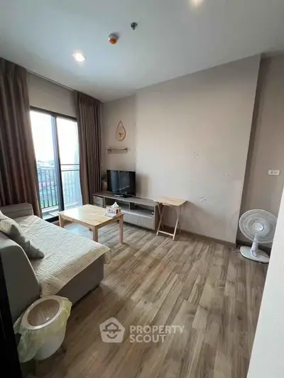 Cozy living room with modern decor and wooden flooring, featuring a comfortable sofa and large window.