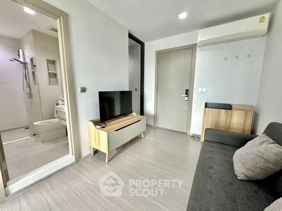 Modern living room with sleek furniture and adjacent bathroom, featuring minimalist design and neutral tones.