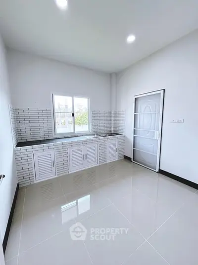 Modern kitchen with sleek white cabinetry and tiled backsplash, featuring ample natural light and minimalist design.