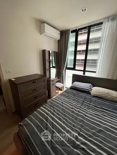 Modern bedroom with striped bedding, dresser, and large window offering natural light.